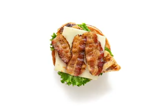 Open sandwich with bacon, cheese, lettuce, and a bun on a white background.