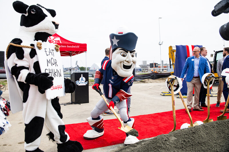 Mascots and individuals at a groundbreaking ceremony with red carpet and shovels.
