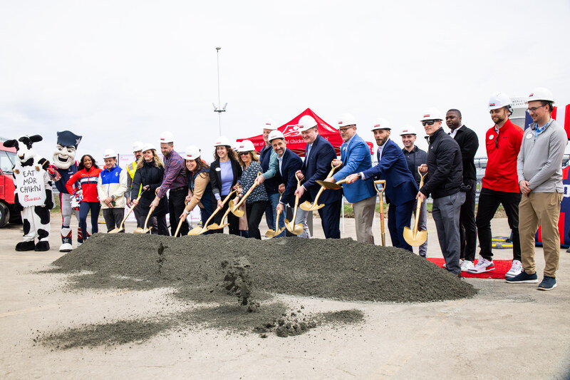 Mascots and a group of people in hard hats participate in a groundbreaking ceremony with shovels.