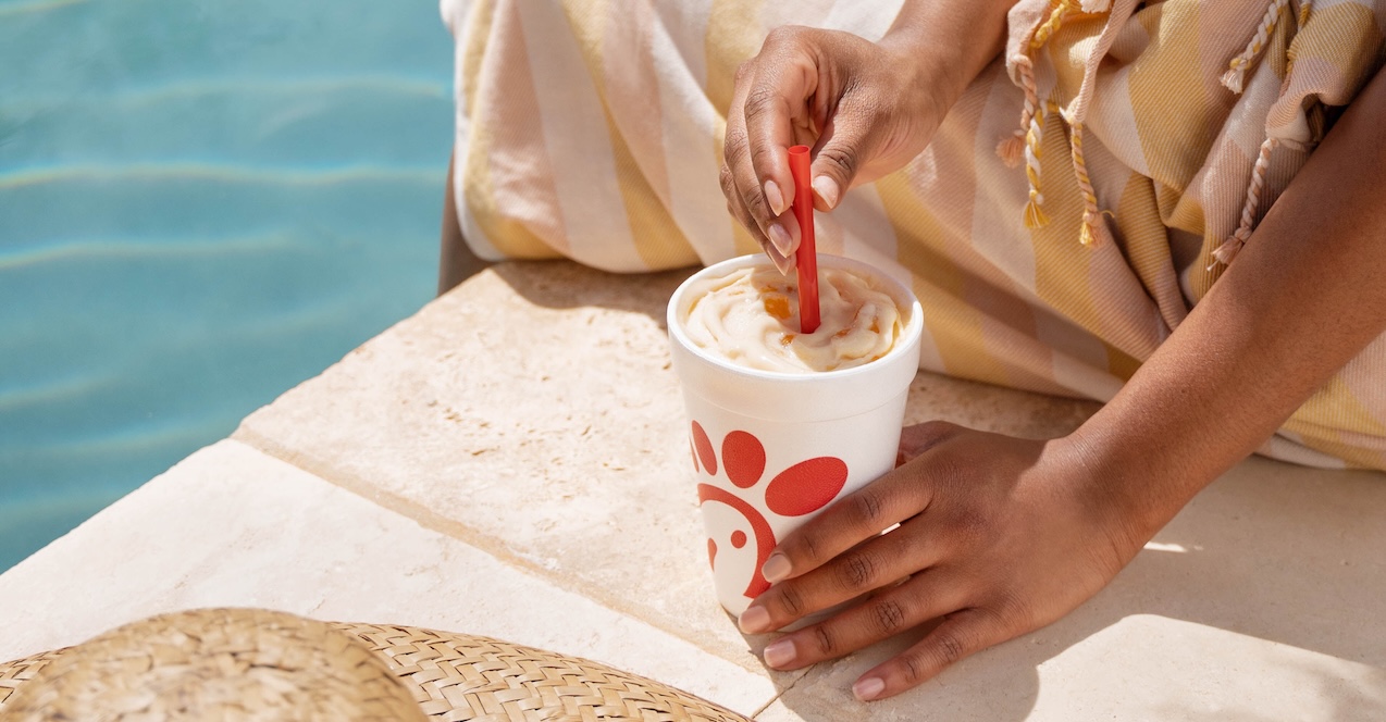 Woman holding Peach Milkshake sitting poolside.