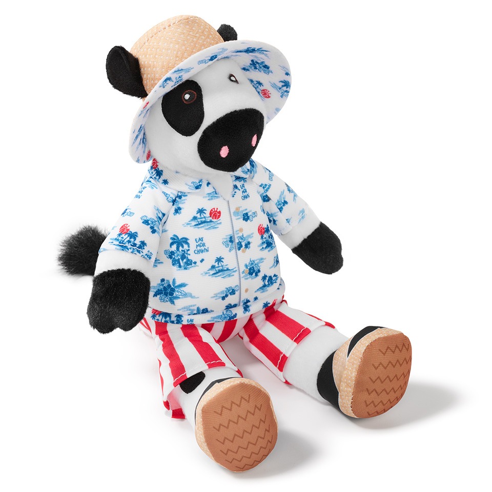 A plush toy cow wearing a straw hat, a blue patterned shirt, and red and white striped pants.