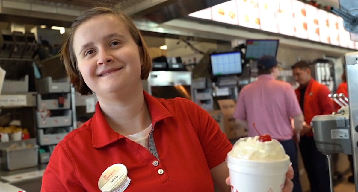 A smiling team member holds a milkshake.