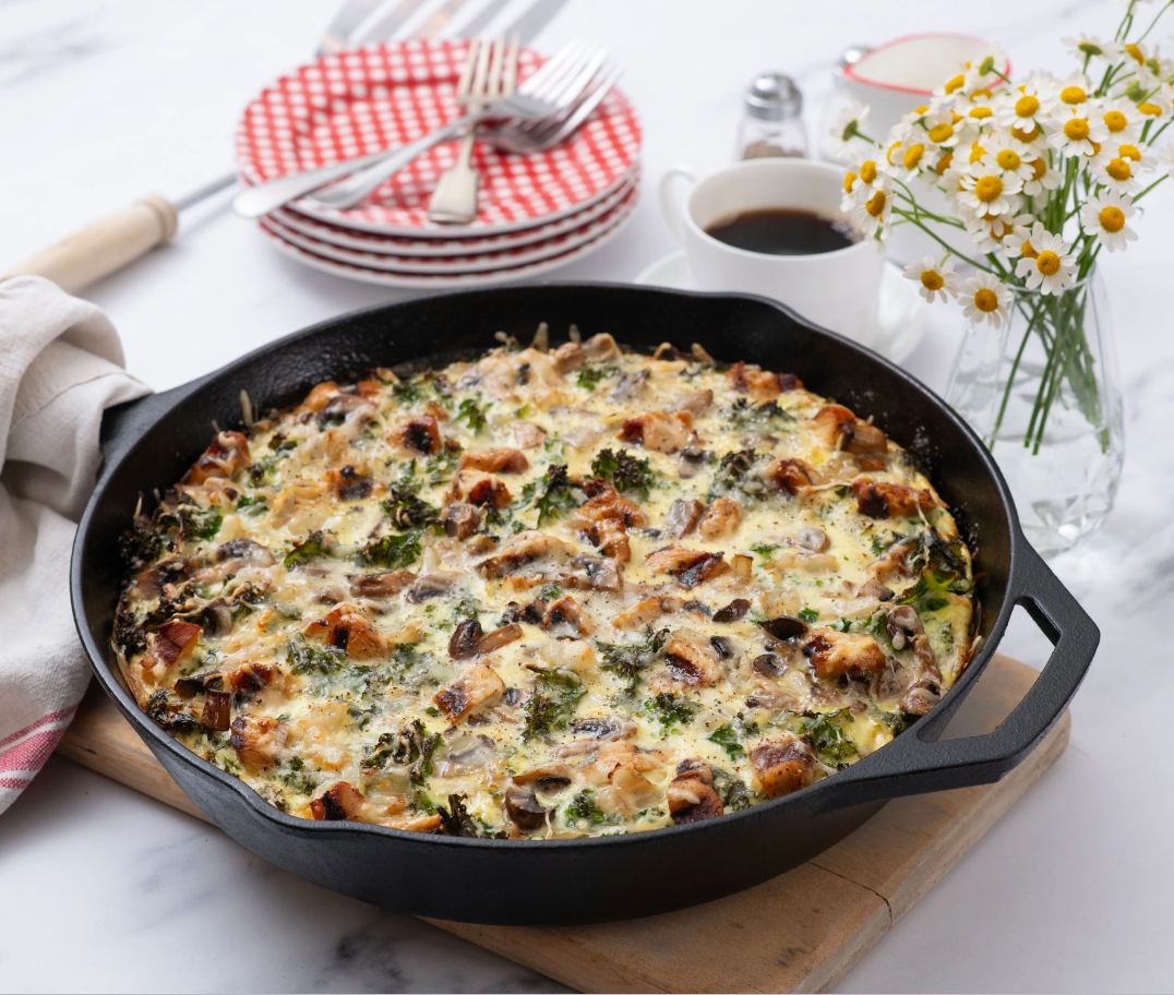 Baked frittata in an iron skillet next to a cup of coffee and flowers in a vase