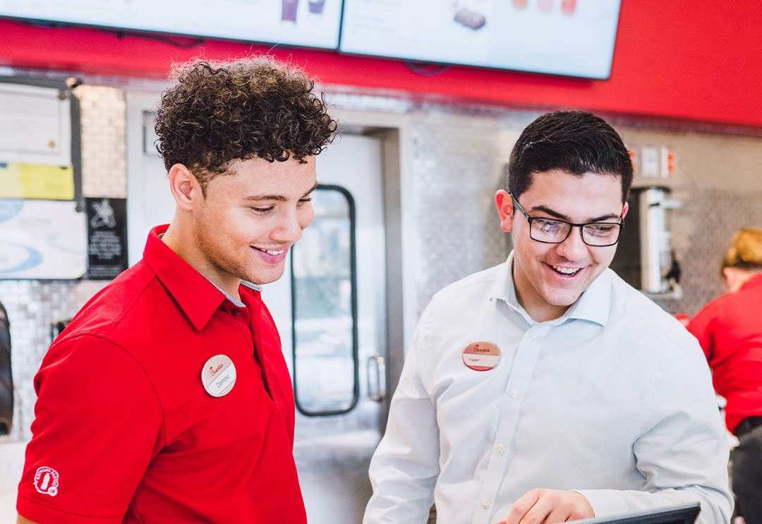 Two team members at Chick-fil-A smiling and conversing at the register.