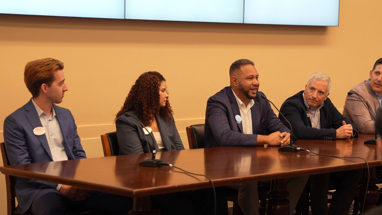 A panel of five people seated at a table during a discussion, with two microphones on the table.