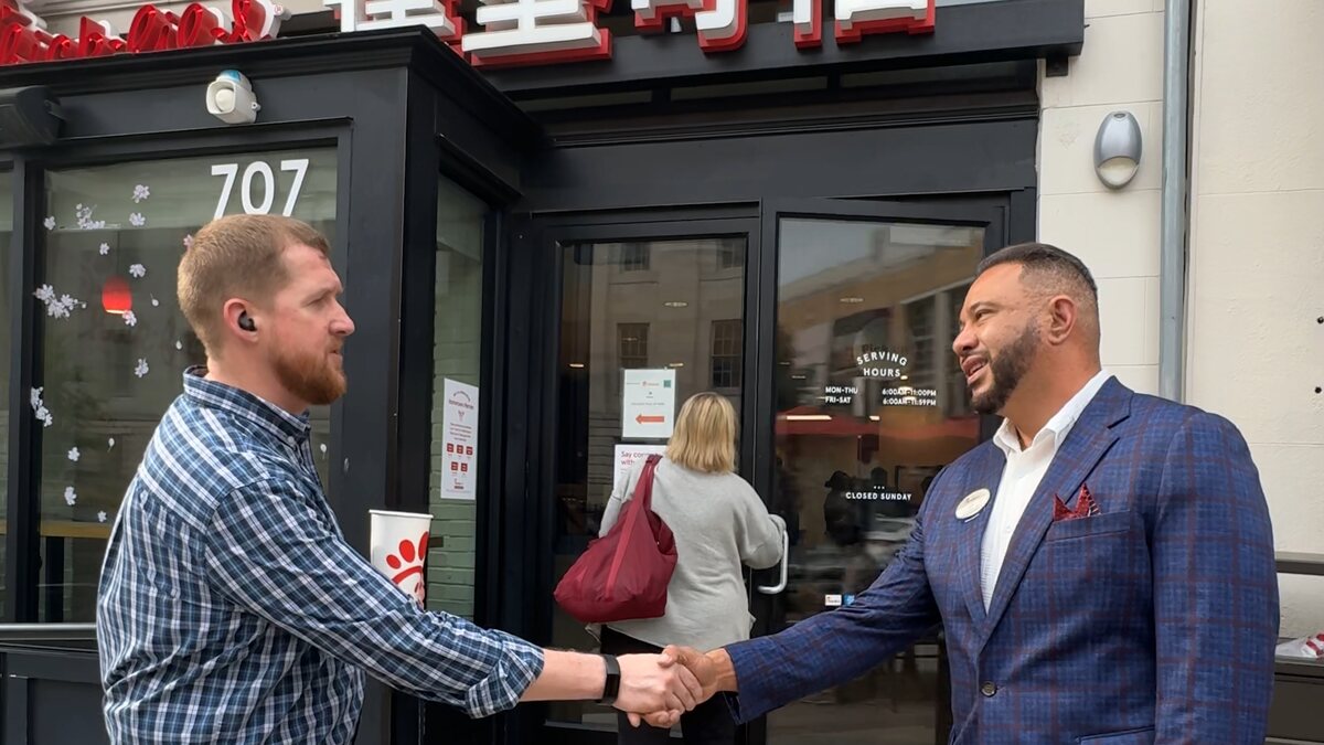 Two men shake hands in front of a Chick-fil-A entrance.

