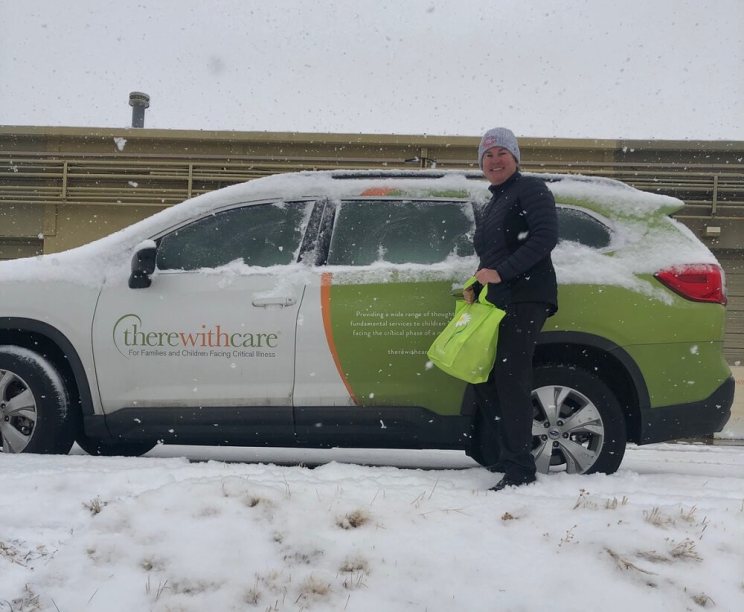 Person standing by a snow-covered SUV with "there with care" logo in snowy weather.