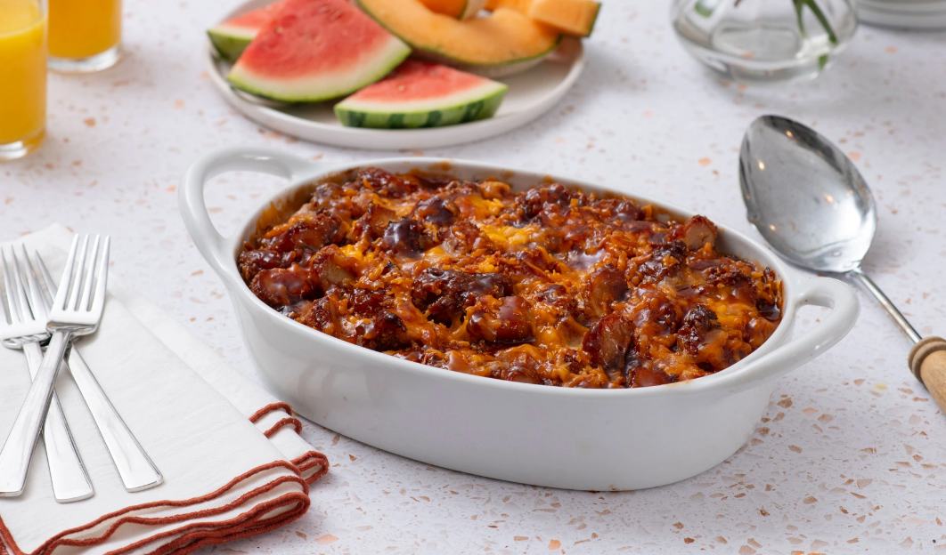 A white ceramic dish of savory Chicken and Egg Breakfast Casserole on a table next to silverware