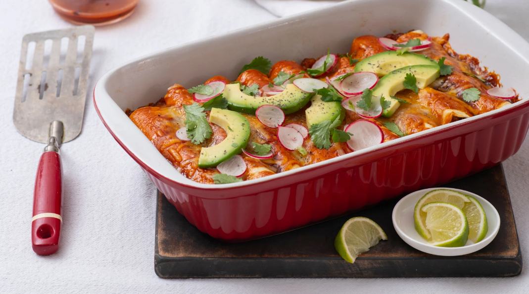 Chicken Enchiladas in a red baking dish garnished with sliced limes