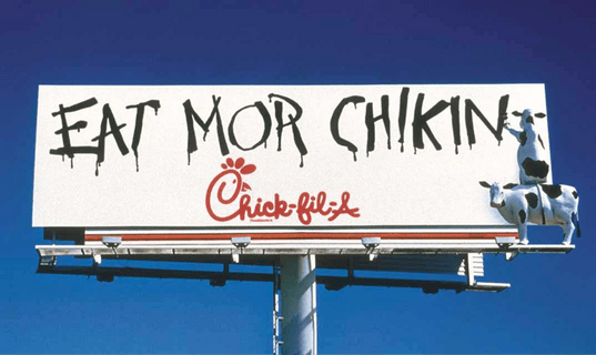 A billboard with the text "EAT MOR CHIKIN" and the Chick-fil-A logo, featuring two cows.