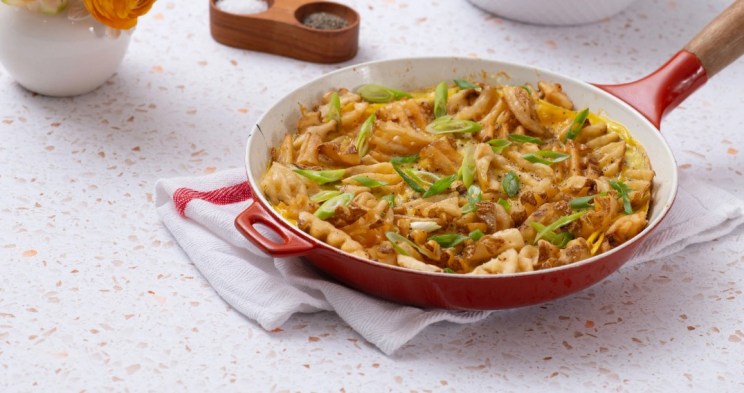 Waffle fry frittata in a red skillet, topped with green onions.