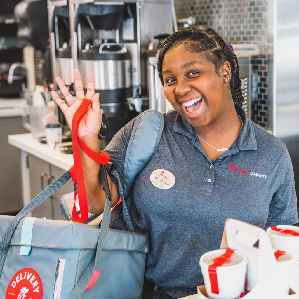 Chick-fil-A® Team Member waving and smiling, holding a delivery bag