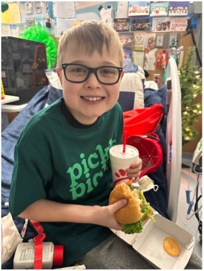 Aidden smiling while holding a Chick-fil-A sandwich and drink.