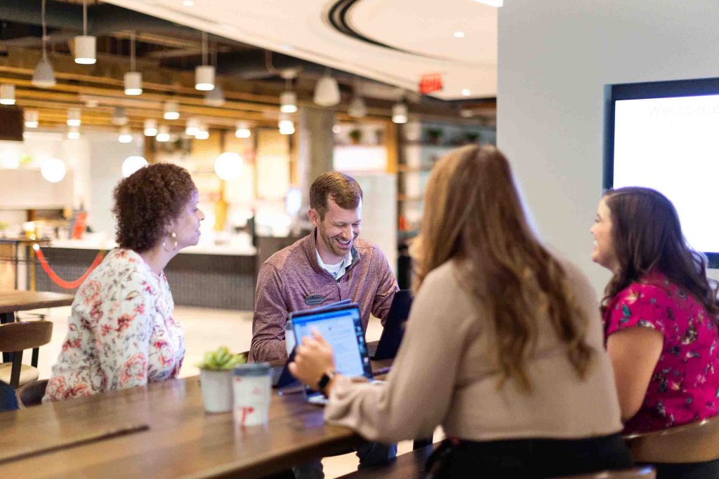 Four people sitting at a table with laptops in a modern setting.

