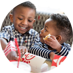 Two young children smiling and eating Chick-fil-A food at a table.
