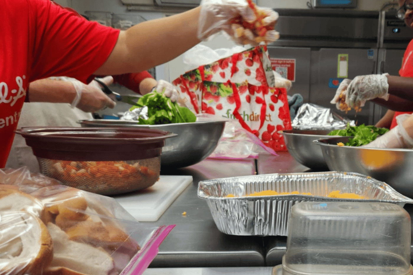 People preparing food at a kitchen counter with bowls of vegetables and ingredients.