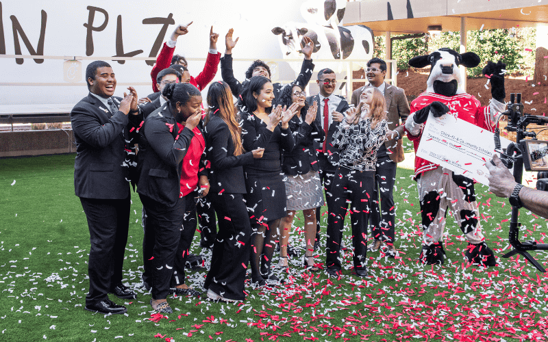 A group of people celebrating with confetti and a person in a cow costume, while someone holds a large check.