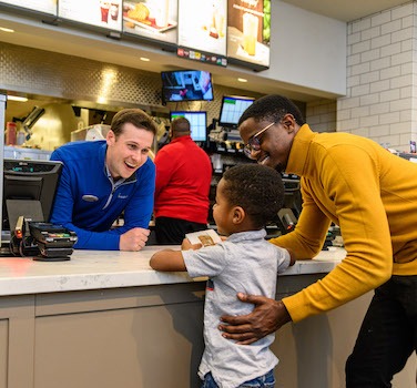 A child and an adult interacting with a smiling Chick-fil-A employee at the counter.