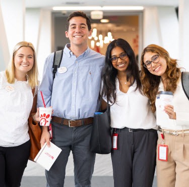 Four young adults standing indoors, smiling, with one holding a Chick-fil-A drink cup.