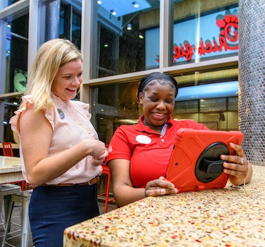 Two women smiling and interacting with a tablet in a bright indoor setting.