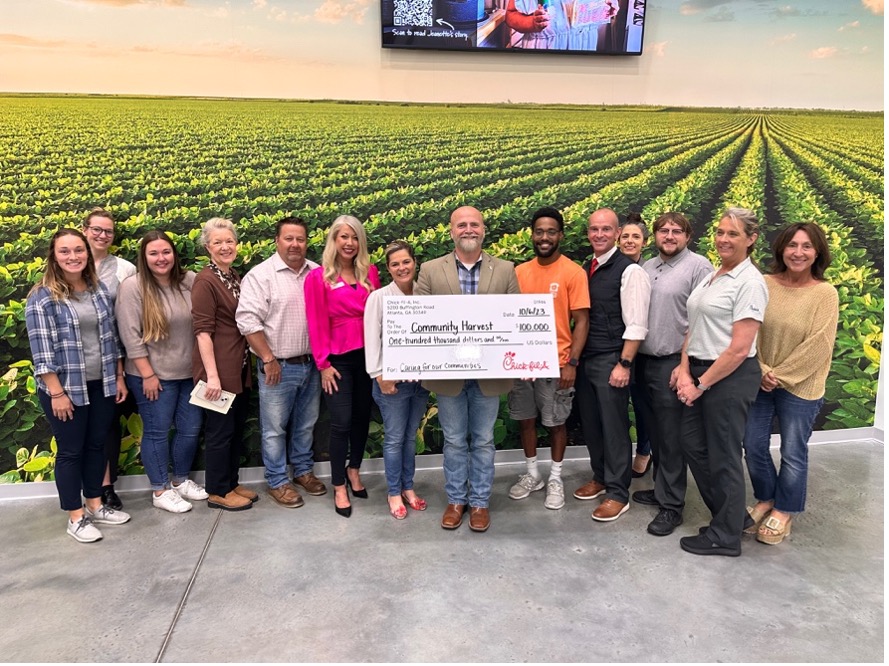 A group of people holding a large ceremonial check in front of a mural of an agricultural field.
