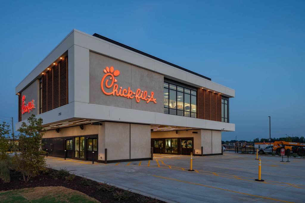 Chick-fil-A exterior at dusk with glowing sign and covered drive-thru lanes.