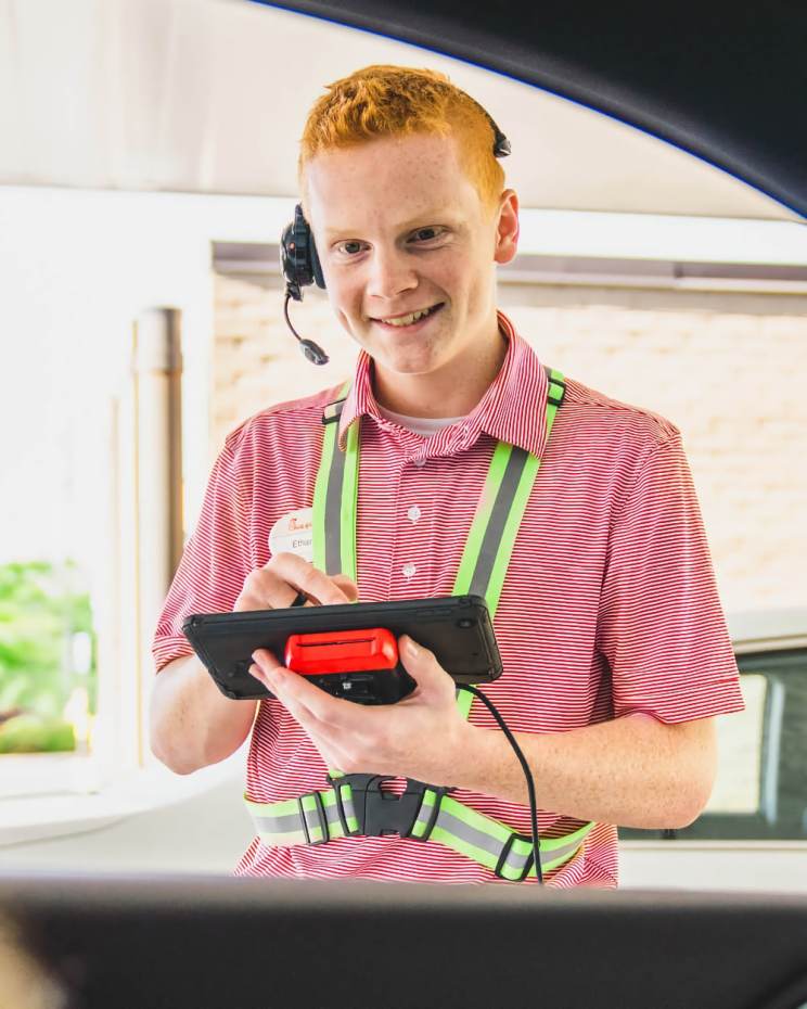 A Chick-fil-A Team member holding a tablet, interacts a customer in the drive-thru.