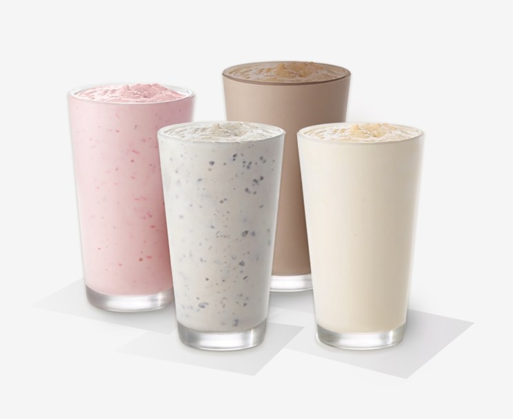 Four tall glasses of milkshakes in different flavors: Cookies & Cream Strawberry, Vanilla, and Chocolate.