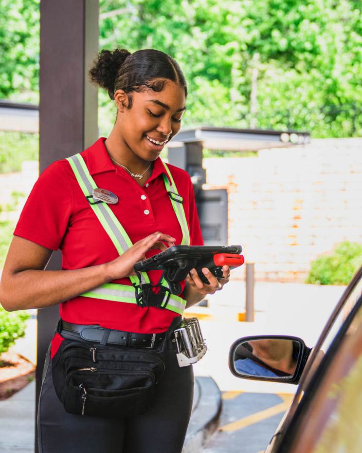 A Chick-fil-A Team member holding a tablet, interacts with a customer in the drive-thru.