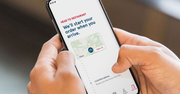 A person holding a smartphone displaying the Chick-fil-A app with the words HEAD TO RESTAURANT We'll start your order when you arrive.