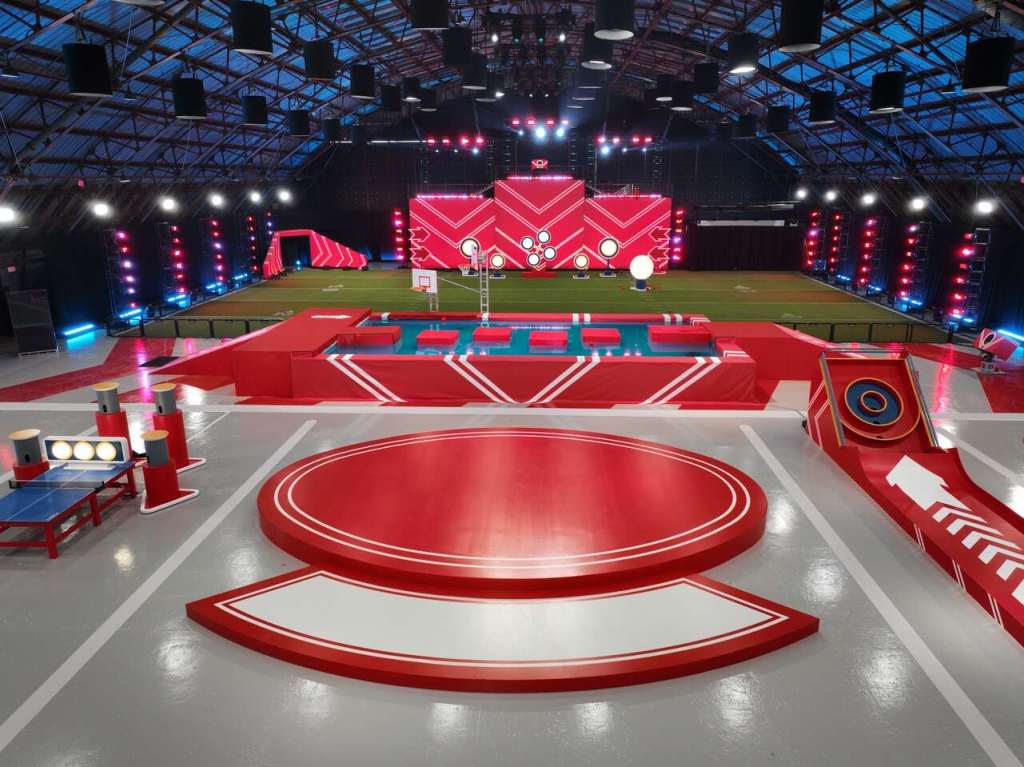 Play it Forward Game Show Challenge with a colorful game setup, featuring a circular platform, obstacle course, and large illuminated screen.