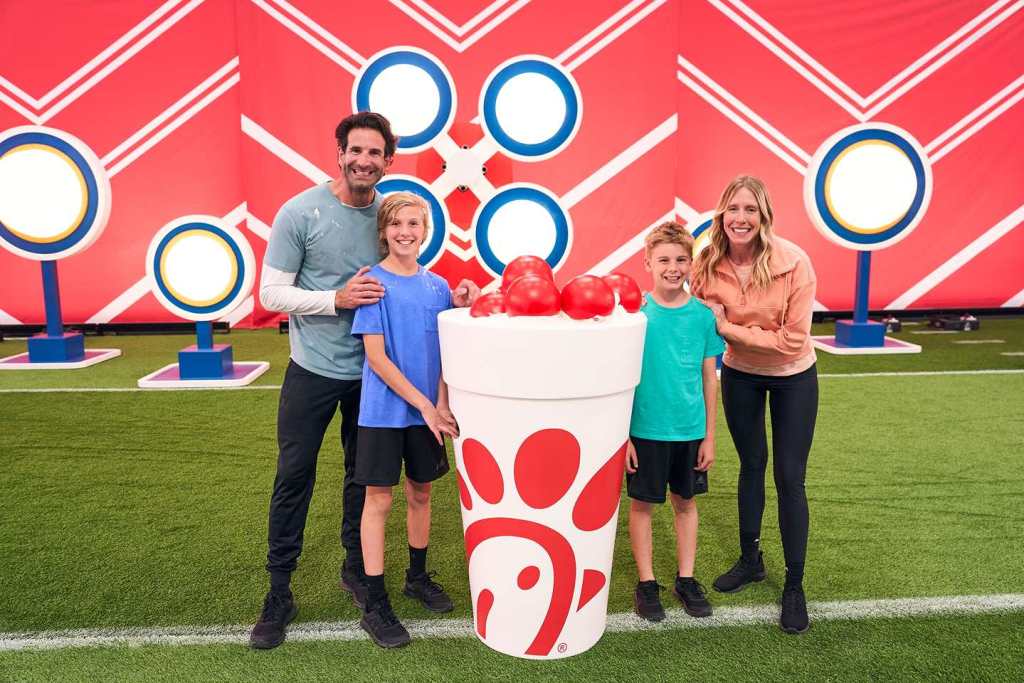 People posing with a large Chick-fil-A cup filled with red balls, set against a red backdrop with targets.