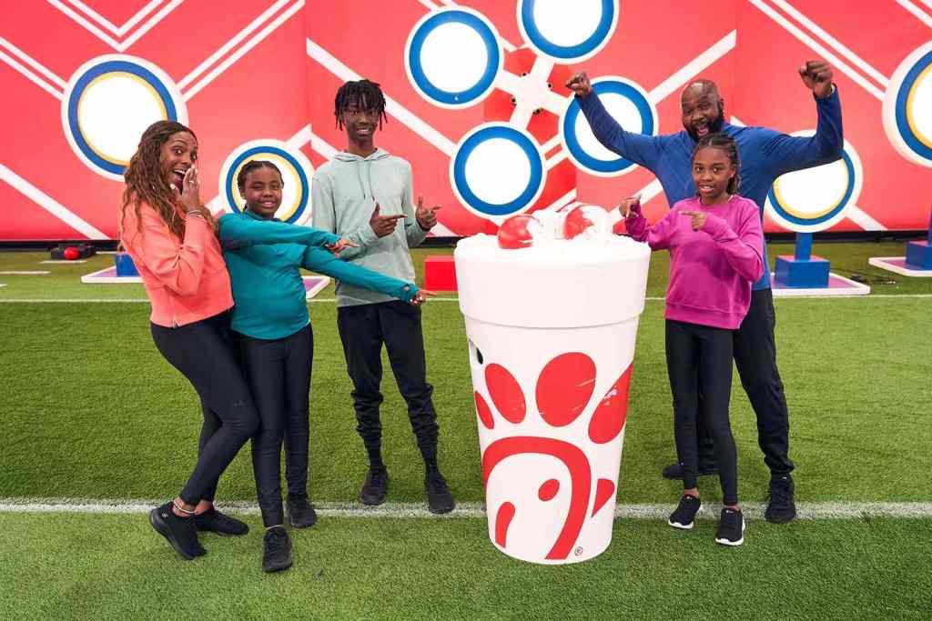 People celebrating with a large Chick-fil-A cup filled with red balls, set against a red backdrop with targets.

