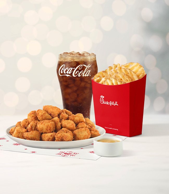 30-ct Chick-fil-A Nuggets sitting on holiday-themed parchment paper, next to a glass of Coca-Cola® and a carton of Waffle Fries with twinkling holiday lights in the background