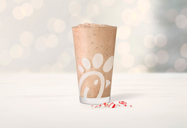 A glass of Peppermint Chip Frosted Coffee next to pieces of peppermint with twinkling holiday lights in the background