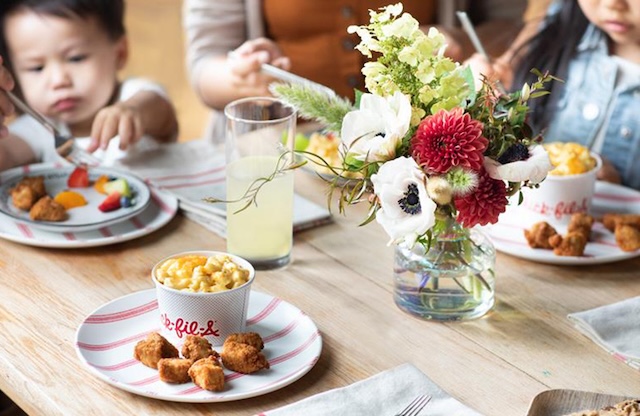 A table with plates of Chick-fil-A food from a Family Style meal with children and parents around it