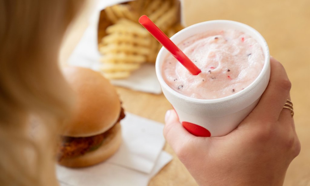 Person holding a Peppermint Chip Milkshake with a Chick-fil-A® Chicken Sandwich and Waffle Fries in the background