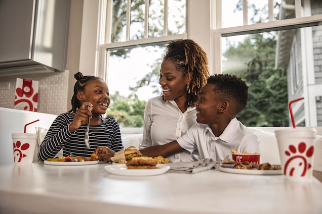 An adult and two children sitting behind a table with Chick-fil-A food