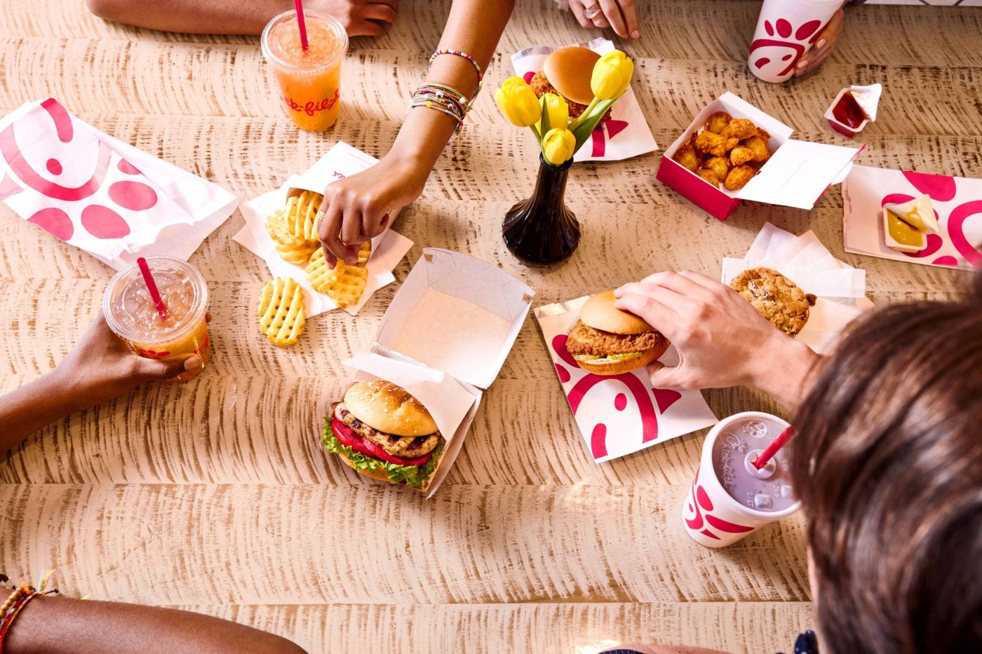 People reaching around a table with Chick-fil-A Waffle Potato Fries®, a Grilled Chicken Sandwich, a Chick-fil-A® Chicken Sandwich and Chick-fil-A® Nuggets