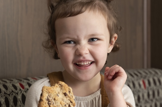 A young child smiling and holding a Chocolate Chunk Cookie