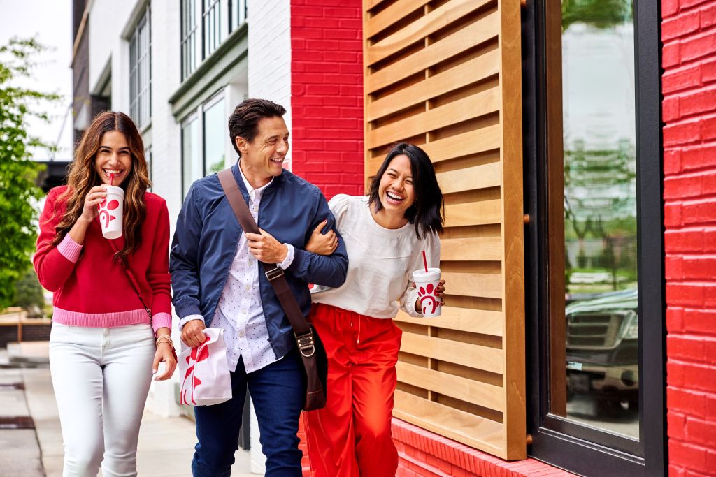 Three people walking together outside, two people holding Chick-fil-A beverages and the other person holding a bag of Chick-fil-A food