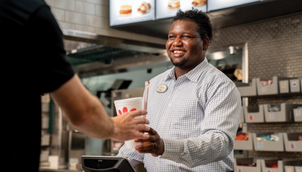 Restaurant Director standing behind the counter, handing a beverage to a customer