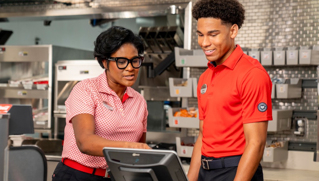 Restaurant Manager standing behind the counter, showing a Team Member how to operate the register