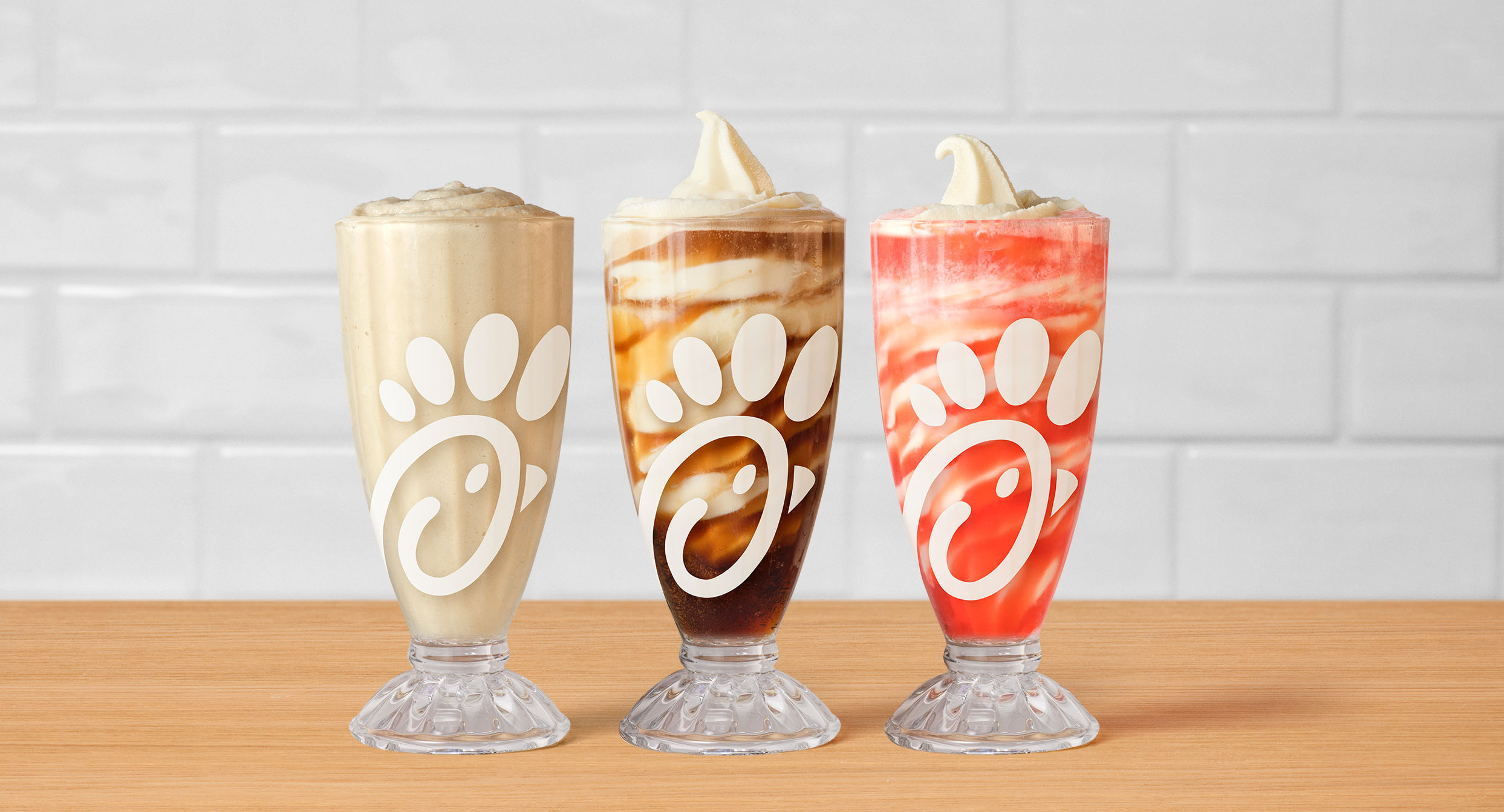 Chick-fil-A's Frosted Soda's and Floats in a row of 3 glasses sitting on a table.