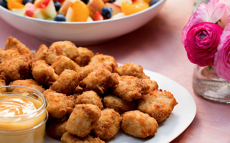 Chick-fil-A® Nuggets Tray on a white plate with a side of Chick-fil-A® Sauce, a bowl of a Fruit Tray and a case of flowers