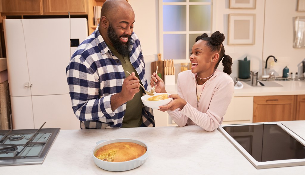 An adult and child standing in front of a kitchen counter, sharing bites of the Chicken Souper Duper Pot Pie