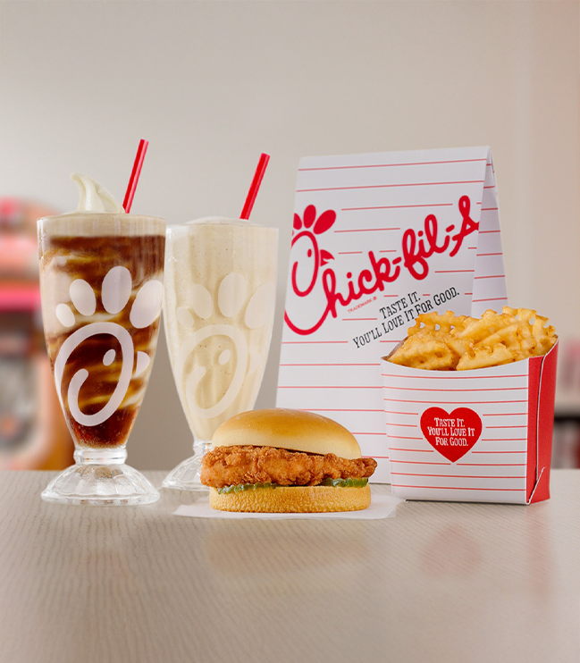 Chick-fil-A® Chicken Sandwich with Waffle Fries, a glass of Frosted Coca-Cola® Soda, a glass of Coca-Cola® Float and a Chick-fil-A bag behind them