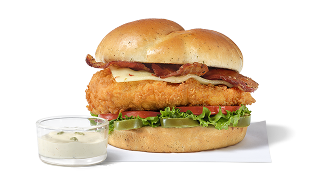 A Jalapeño Ranch Club sandwich with an Original Filet on a white napkin next to a small a glass bowl of Jalapeño Ranch Sauce