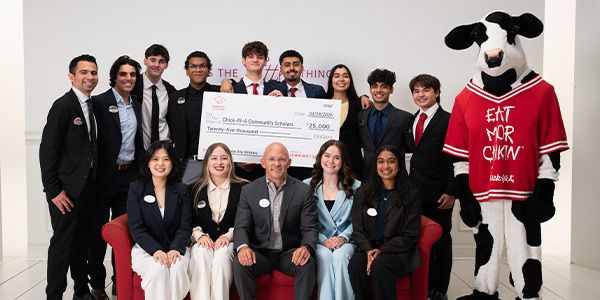 Group of people sitting and standing together on a red couch with a Chick-fil-A Cow and holding a large check