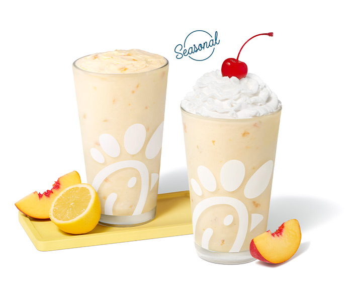 Peach Frosted Lemonade with a peach slice and a lemon half sitting on a tray next to a Peach Milkshake with a peach slice